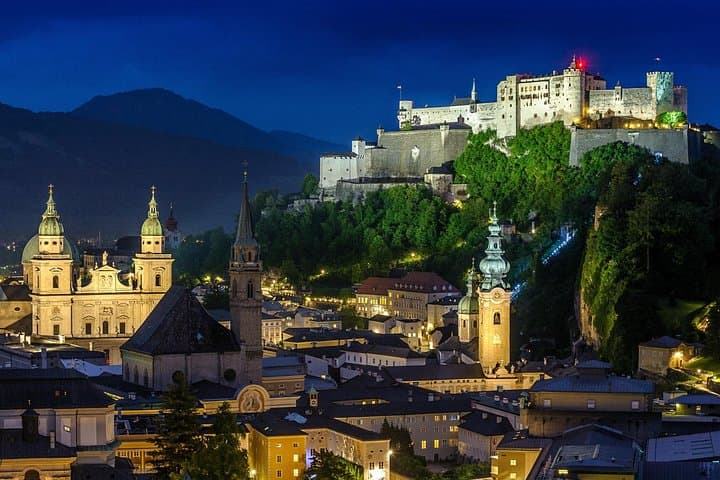Salzburg’s historic Old Town by night, viewed from Mönchsberg. The iconic Hohensalzburg Fortress, Cathedral, and St. Peter’s Abbey rise majestically in the background, creating an unforgettable view.
